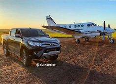 a truck parked next to a small plane on a dirt road in front of a field