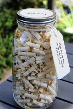 a jar filled with pasta noodles sitting on top of a wooden table next to a green bush