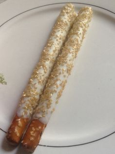 two sticks with gold sprinkles are on a white plate