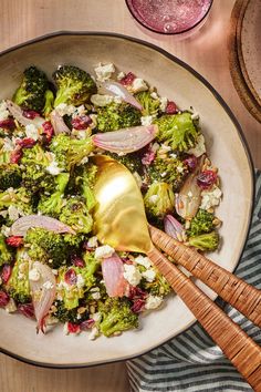 a bowl filled with broccoli and onions on top of a wooden table next to a glass of wine