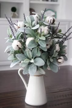 a white pitcher filled with flowers on top of a wooden table