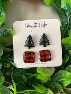 the plaid christmas tree earrings are on display next to some green plants and leaves in front of a white card