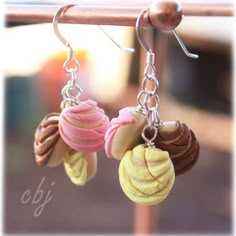 three different colored pastries hanging from silver earwires on a metal hook,