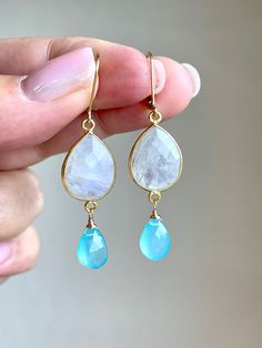 Rainbow Moonstone and Chalcedony Earrings, June Birthstone, White and Aqua Blue Dangle Earrings, Long Gemstone Jewelry, Summer Gift for her These eye catching earrings feature a pair of Rainbow Moonstone elongated teardrop bezeled stones in gold filled. Suspended from them are refreshing Aqua Chalcedony faceted teardrop wire wrapped in gold filled. These white and aqua blue two stone earrings are very light weight, neutral yet classic, elegant and timeless. These earrings can be dressed up or down and have a beautiful color combination that makes them suitable for multiple outfits.  Ideal gift for a women born in June, as Rainbow Moonstone is the birthstone of the month of June About These Earrings: - Gemstone: Rainbow Moonstone and Aqua Chalcedony - Birthstone: June - Moonstone Properties Blue Moonstone Earrings With Natural Stones, Blue Moonstone Drop Earrings, Blue Teardrop Moonstone Jewelry, Teardrop Blue Moonstone Jewelry, Blue Moonstone Jewelry With Matching Earrings, Moonstone Properties, Multiple Outfits, Chalcedony Earrings, Blue Dangle Earrings