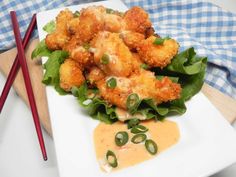 a white plate topped with lettuce covered in sauce next to chopsticks