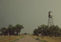 an old water tower on the side of a road with trees in the foreground