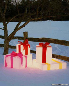 three gift boxes with red bows are in the snow near a tree and fence on a snowy day