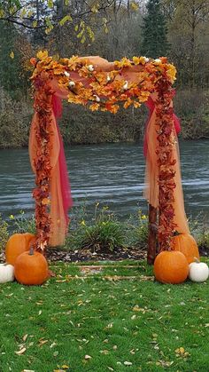 an outdoor ceremony set up with pumpkins and flowers on the grass next to water