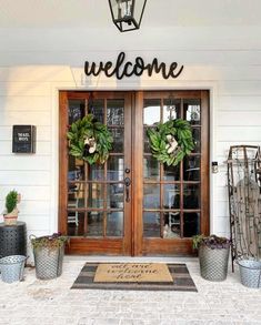 a welcome sign on the front door of a white house with potted plants and wreaths