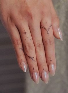 a woman's hand with two small tattoos on her left thumb and one finger