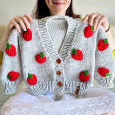 a woman holding up a knitted sweater with strawberries on it