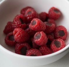 some raspberries are in a white bowl