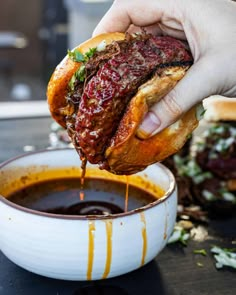 a person dipping sauce onto a sandwich in a bowl