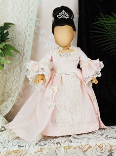 a doll in a pink dress and tiara sitting on a table next to a potted plant