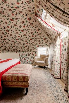 a bed sitting under a window in a bedroom next to a chair and wall paper