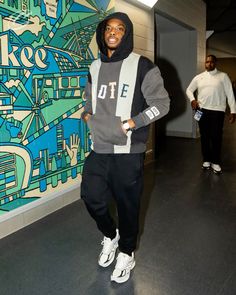 a man standing in front of a colorful wall with his hands on his hips and wearing a hoodie