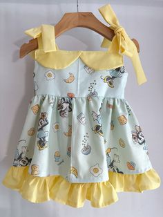 a yellow and white dress with mickey mouses on it, hanging from a wooden hanger