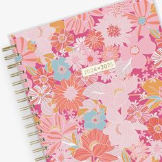 a pink and orange flowered notebook with a gold sticker on the front cover