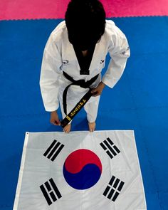 a man standing on top of a blue and white floor holding a black belt in front of a flag