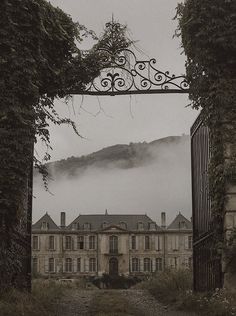 an old building with a gate in front of it and fog rolling over the mountains