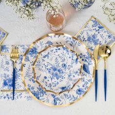 a blue and white place setting with gold trimmings on the edge, along with silverware