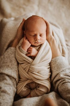 a newborn baby wrapped in a blanket is being held by someone's hands while laying down