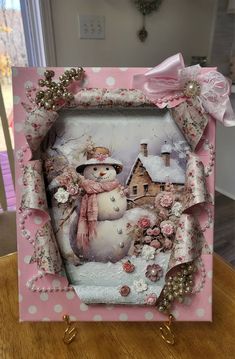 a pink frame with a snowman in the middle and a house on it's side