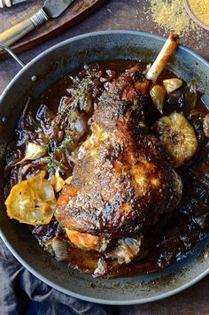 a pan filled with meat and spices on top of a wooden table next to utensils