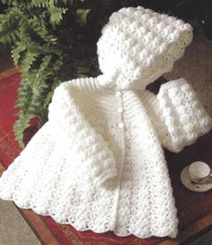 a crocheted white coat and hat sitting on top of a table next to a potted plant