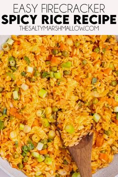 a bowl filled with rice and vegetables on top of a white table next to a wooden spoon