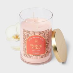 a pink candle with a gold lid next to a white orchid flower on a gray background