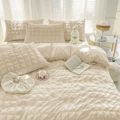 a bed with white comforters and pillows on top of it next to a window