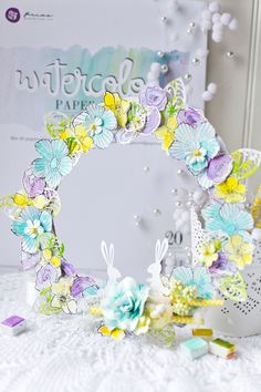 an easter wreath made out of paper flowers and other items on a table with a sign in the background