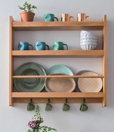 a wooden shelf filled with plates and cups on top of a table next to a potted plant