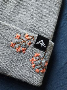 a gray sweater with orange flowers on the front and side, sitting on a blue surface