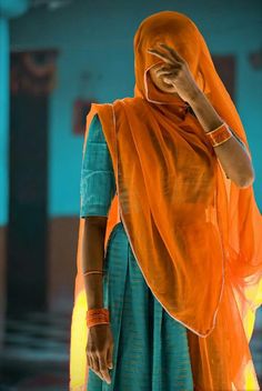 a woman in an orange scarf is talking on her cell phone while wearing a blue dress