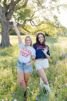 two girls standing in the grass with their arms up