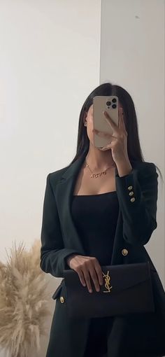 a woman taking a selfie in front of a mirror wearing a black suit and gold accessories