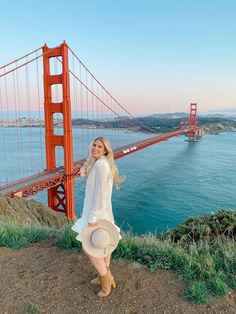 a woman standing in front of the golden gate bridge with her hat on and looking at the camera