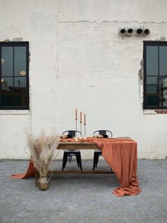 the table is set with two black chairs and an orange cloth draped over it, along with candles