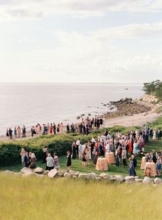 a group of people standing on top of a lush green field next to the ocean