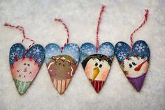 four ornaments in the shape of hearts with snowflakes on them, hanging from red and white twine