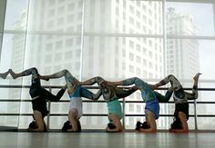 five people doing handstands in front of a large glass window with buildings in the background