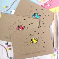 three cards with birds on them sitting next to a pencil and some confetti