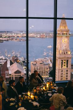 a group of people sitting at a table in front of large windows with city lights on them