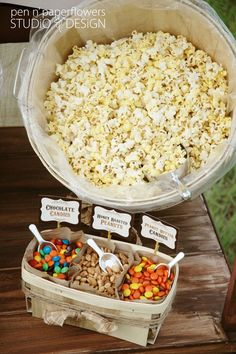 popcorn and other snacks are sitting in plastic containers on a table with name tags attached to them