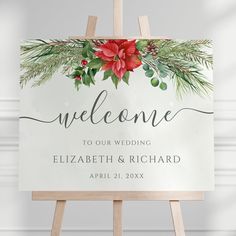 a welcome sign with red flowers and greenery on it, sitting on an easel