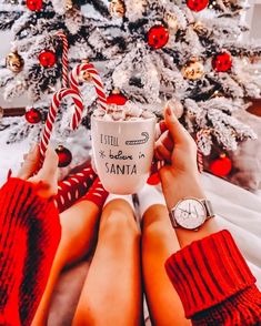 two people sitting in front of a christmas tree with their feet on the coffee cup