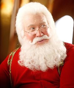 an old man dressed as santa claus sitting in front of a christmas tree and looking at the camera