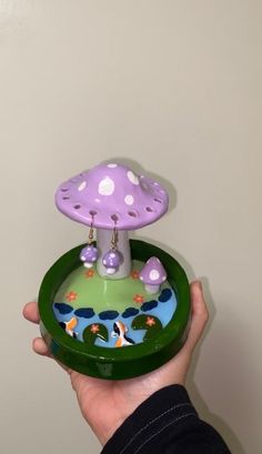 a hand holding a green tray with a purple mushroom on it and white polka dots